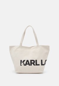 Beżowa torba płócienna z dwoma uchwytami i dużym czarnym napisem "KARL L" częściowo widocznym z przodu.