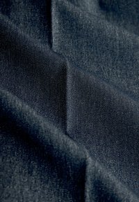 Tumši denima audums ar gludu tekstūru, kas ir zilgani pelēkā krāsā un ar viegli diagonālām aušanām. Materiāls ir salocīts, atklājot dziļumu.