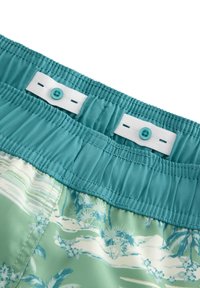 Pantaloni da bagno turchesi con cintura elastica, dotati di chiusura a bottone e un motivo floreale tropicale nelle tonalità di verde chiaro e blu.