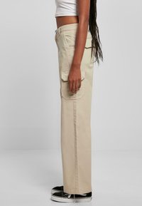 Pantalones cargo beige con un diseño de pierna recta, bolsillos laterales y cierre de botón, combinados con zapatillas negras.