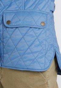 Himmelblaue gesteppte Jacke mit Rautenmuster, ausgestattet mit einer Klappentasche, Messingdruckknöpfen und dem gestickten Markennamen "Barbour".