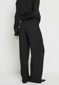 Zwarte broek van lichtgewicht stof, met een losse pasvorm, recht gesneden pijpen en een gladde textuur. Eenvoudig, zonder zichtbare patronen of accenten.