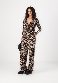 Mono de estampado de leopardo con mangas largas, escote en V profundo y piernas anchas; hecho de tela suave, cuenta con detalles en negro y zapatos de plataforma planos.