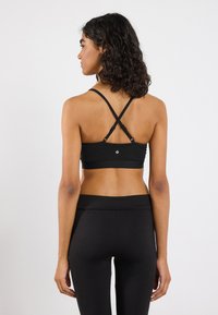 Zwarte sportbeha met kruisbanden en een gladde textuur. Heeft een klein logo op de achterkant, gecombineerd met bijpassende zwarte legging.