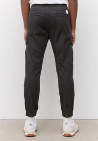 Černé cargo kalhoty s elastickým pasem, bočními kapsami, zúženými manžetami a hladkou texturou. V kombinaci s bílými teniskami a vzorovanými ponožkami.