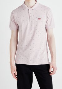 Světle růžové polo tričko s límečkem, zdobené malými námořnicko-modrými a bílými tečkami, se třemi knoflíky a červenou nášivkou s logem Levi's.