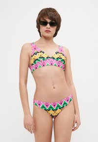 Multifarvet bikini sæt med et levende geometrisk mønster i pink, grøn, sort og gul. Blødt stof, bralette-top med brede stropper.