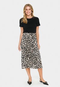 Haut noir à manches courtes associé à une jupe midi à imprimé léopard beige. La jupe présente un design fluide et une taille élastique, complétée par des chaussures noires.