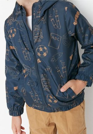 Navy windbreaker with orange line drawings of robots, soccer balls, science elements, and school items; zip closure and elastic cuffs.