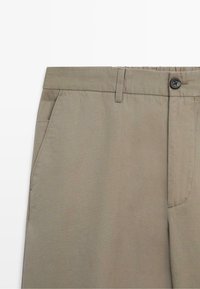 Pantalon beige en coton avec poches latérales avant, passants de ceinture et fermeture à bouton noir à la taille.