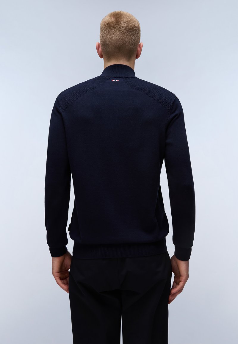Pull en maille bleu marine pour homme avec col montant, poignets côtelés et un discret logo au niveau du cou. Le tissu semble lisse et ajusté.