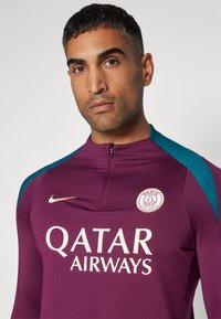 Violetti urheilupaita, jossa on turkoosit olkakoristeet, korkea kaulus ja puolivetoketju. Rinnassa on "Qatar Airways" -logo ja PSG:n vaakuna.