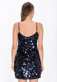 Granatowa sukienka z cekinami o dopasowanym kroju, regulowanych ramiączkach typu spaghetti i wycięciem na plecach. Gładka faktura z okrągłymi, błyszczącymi zdobieniami.
