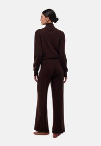 Ensemble en tricot marron à deux pièces avec un col montant et des manches longues, comprenant un pantalon ample ; texture douce, design minimal, vue de dos.