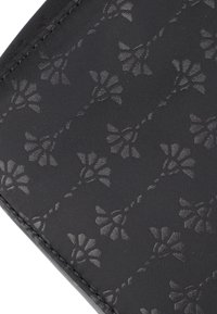 Tessuto nero testurizzato con un sottile motivo floreale, con steli e fiori intrecciati che decorano la superficie.