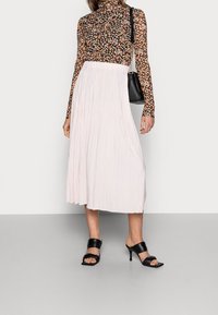 Top floreale a maniche lunghe con sfondo nero, abbinato a una gonna midi plissettata di un rosa chiaro e sandali con tacco alto neri.