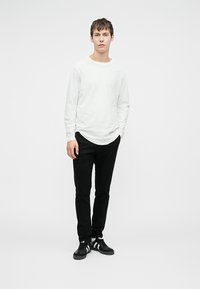 Hvid langærmet t-shirt sammen med sort slim-fit bukser og sorte sneakers med tre hvide striber langs siden.