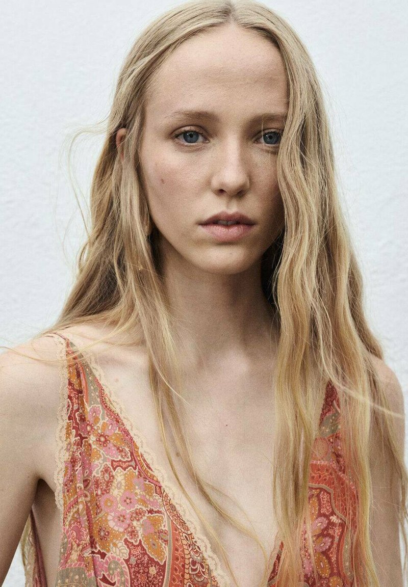 Vestido largo en tejido ligero, con un patrón floral en tonos rojos, rosas y terrosos. Un borde de encaje en el escote realza la textura.