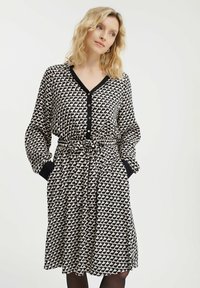 Sukienka z długim rękawem w kolorze czarnym i kremowym, z powtarzającym się geometrycznym wzorem, z przodem na guziki oraz ściągniętą talią z wiązaniem. Z akcentowanymi mankietami.