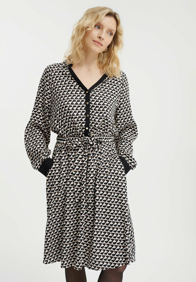 Sukienka z długim rękawem w kolorze czarnym i kremowym, z powtarzającym się geometrycznym wzorem, z przodem na guziki oraz ściągniętą talią z wiązaniem. Z akcentowanymi mankietami.