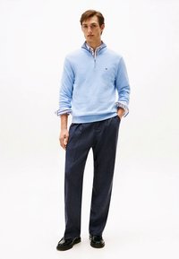 Light blue zip-up sweater over a collared shirt, paired with dark tailored trousers and black shoes. Smooth texture, classic design.