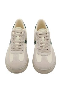 Zapatillas beige con acentos verdes, hechas de ante y tejido. Punta redondeada, cierre con cordones y cuello acolchado para mayor comodidad.