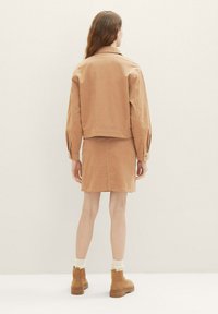 Veste en denim beige avec une coupe courte, associée à une jupe assortie de couleur beige. Les deux articles présentent une texture douce et un design minimaliste. Les bottes sont beiges avec une semelle épaisse.