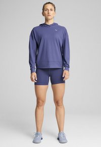 Hanorac cu glugă de culoare mov, cu mâneci lungi, asortat cu șorturi mov și adidași de culoare albastru deschis. Material moale, croială relaxată.