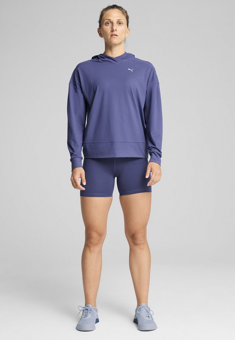 Lilla hoodie med lange ærmer, parret med matchende lilla shorts og lyseblå sneakers. Blødt stof, afslappet pasform.