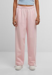 Lyserøde sweatpants med elastisk talje og justerbare manchetter, lavet af blødt materiale. Sat sammen med hvide sneakers.