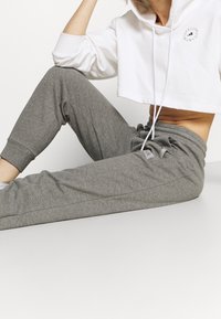 Grijze joggerbroek met elastische boorden, voorzien van een koord in de taille. Gecombineerd met een korte witte hoodie met een logodetail.