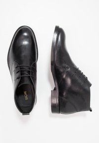 Černé kožené kotníkové boty na šněrování s hladkým povrchem, jedna zobrazená shora a druhá z boku na bílém pozadí.