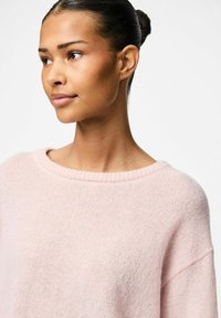 Ljust rosa oversized tröja i mjukt, texturerat garn. Har en bred halsringning och detaljer med ribbad mudd. Minimalistisk design.