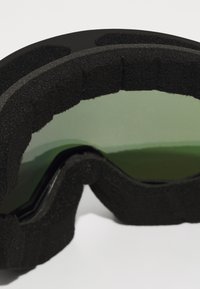Lunettes de ski noires avec une forme courbée, rembourrage en mousse autour des bords et lentilles teintées de vert reflétant la lumière. Fini de surface texturé.