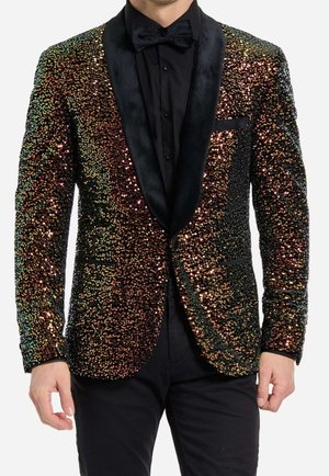 Homme portant une veste de smoking noire ornée de sequins multicolores, associée à une chemise noire et un nœud papillon noir.