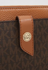 Brunt læderpung med en struktureret finish, der har et guldrund logo og en stofpanel med et monogrammønster i mørkebrun.