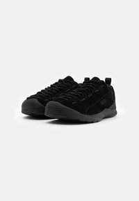 Czarne buty sportowe wykonane z zamszu z teksturowaną gumową podeszwą, charakteryzujące się niskim profilem, zaokrąglonym noskiem i płaskimi sznurówkami.
