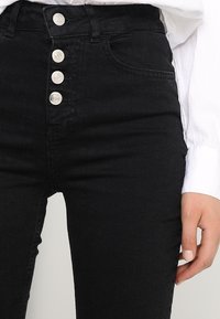 Černé džíny s vysokým pasem vyrobené z denimu, s pěti stříbrnými knoflíky a předními kapsami. Hladká textura s mírným elastickým efektem.