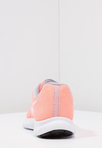 Chaussure de sport en maille rose avec des accents gris, un col rembourré et une semelle blanche. Surface texturée et design léger.