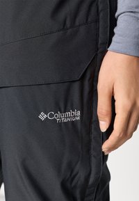 Fekete Columbia Titanium nadrág sima textúrával, ferdefelvágású oldalzsebbel és hímzett logóval a combon.