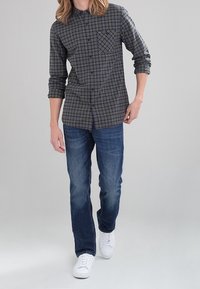 Geruit overhemd met knopen in groen, grijs en zwart, voorzien van een borstzak. Gepaard met blauwe jeans en witte sneakers.