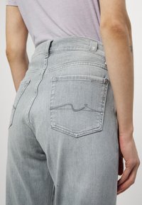 Jean gris délavé taille haute, avec des poches arrière dotées d'un subtil détail de couture et d'une étiquette sur la taille. Texture de denim lisse.
