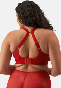 Sostén rojo con tirantes ajustables y cierre de gancho y ojal. Tejido suave con un diseño sin costuras, enfatizando comodidad y soporte.