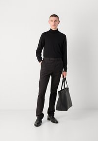 Zwarte coltrui, slim zwarte broek en zwarte leren schoenen. Houdt een zwarte leren schoudertas vast. Eenvoudig, minimalistisch ontwerp.