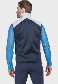 Blaue Sportjacke mit hellblauen und dunkelblauen Paneelen, ausgestattet mit hohem Kragen, strukturierten Ärmeln und tailliertem Schnitt.