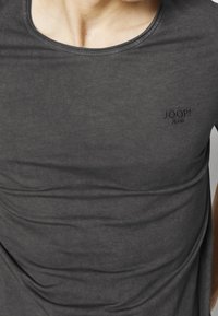 Primo piano di una persona che indossa una maglietta grigia scura di Joop! Jeans con scollo rotondo e area del petto visibile.