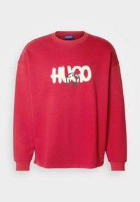 Sweat-shirt rouge à manches longues avec col rond et texte graphique blanc "HUGO" sur la poitrine.