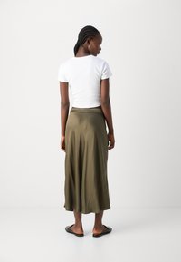 Valkoinen lyhythihainen crop-top yhdistettynä pitkään oliivinvihreään satiinishortsiin. Asusteessa on rento istuvuus ja sileä, virtaava rakenne.