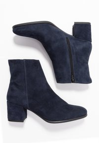Bottines en daim bleu marine avec talon bloc, fermeture éclair latérale et bout arrondi. Texture lisse avec détails de couture visibles.