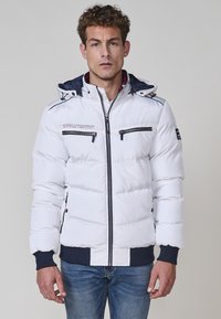 Chaqueta acolchada blanca con capucha, que cuenta con bolsillos con cremallera en el pecho, acentos en azul y puños acanalados. Textura suave, diseño acolchado.